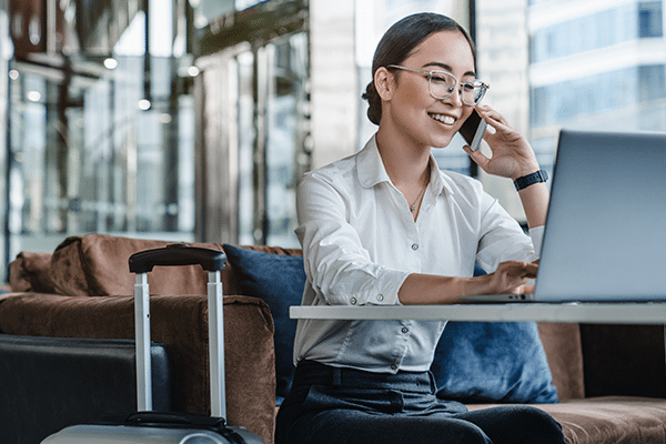 Asian female sitting at airport before trip having telephonic conversation with client and smiling