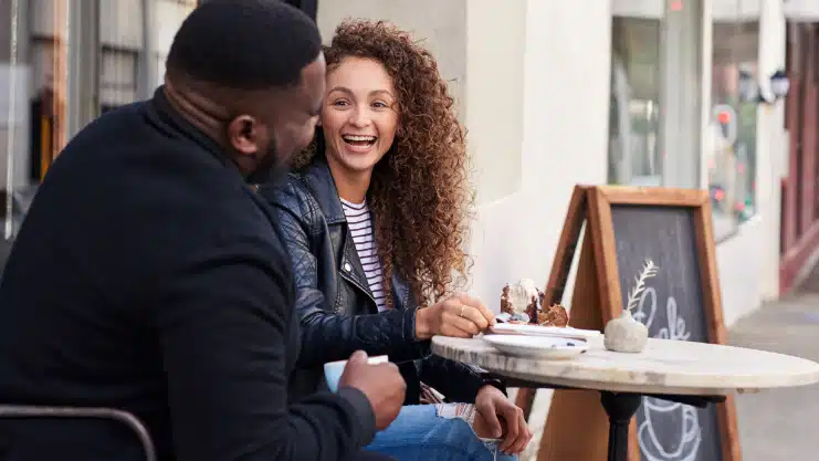 Two smiling friends talking together at a sidewalk cafe cropped